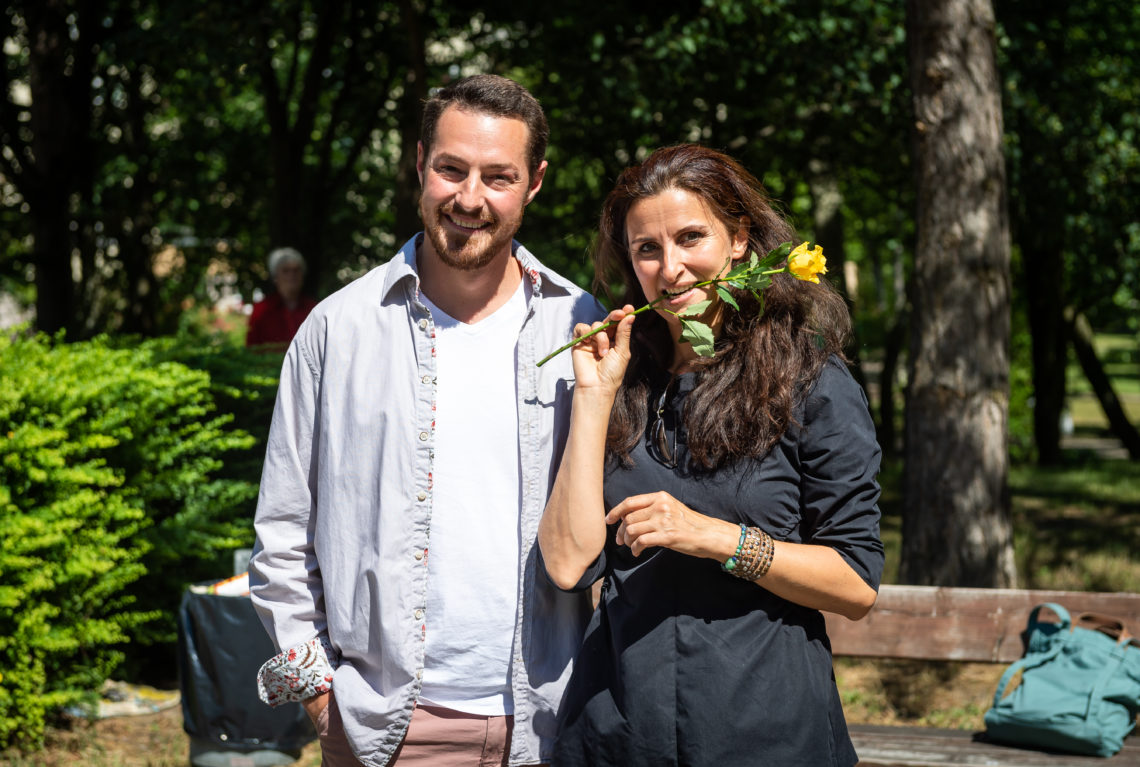 Eine Frau im Kleid mit einer Rose im Mund neben einem Mann.