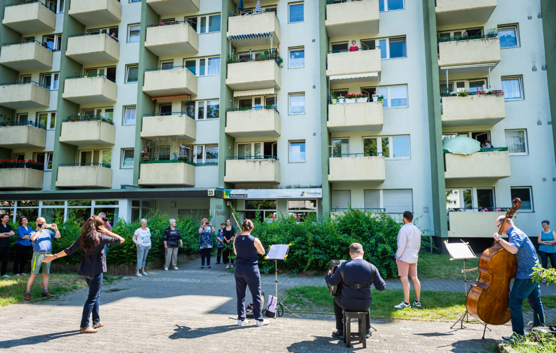 Musikanten spielen vor einem Plattenbau Musik für die AnwohnerInnen.